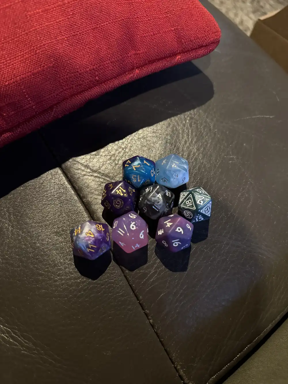 A set of 8, 20-sided resin dice on a couch, in various styles.